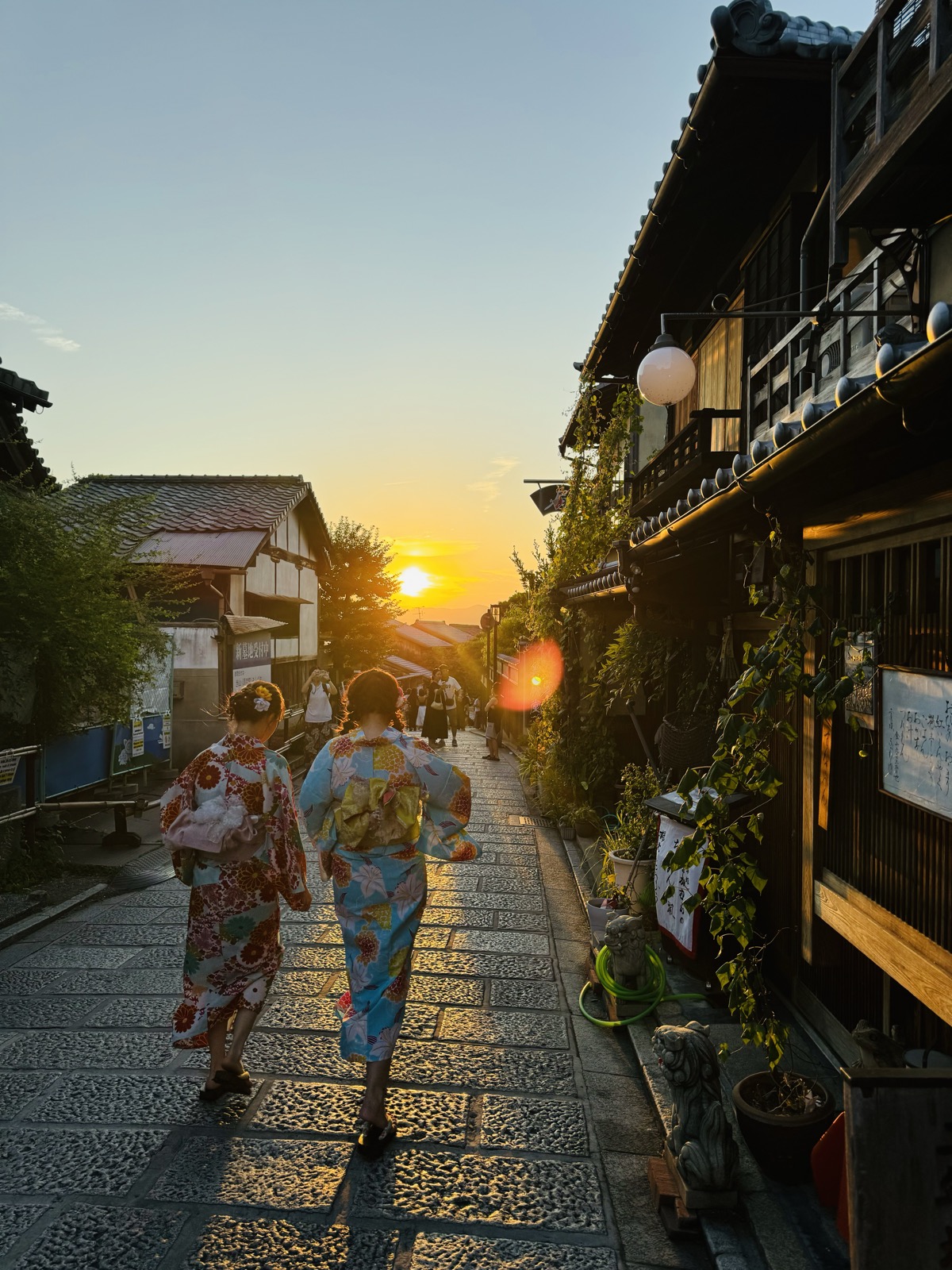 Two people in rented kimono walking down the stone slope of Ninenzaka toward a low Kyoto sun