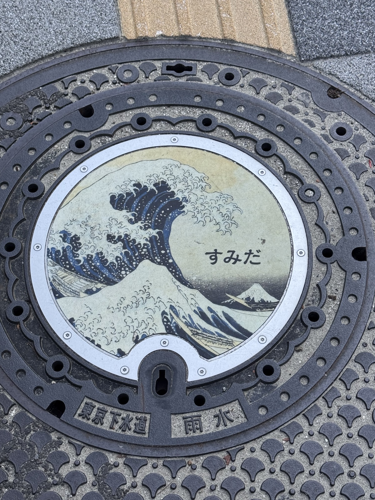 A manhole cover painted with Hokusai's Great Wave and the word Sumida